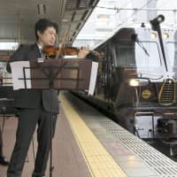 A violinist and pianist perform alongside Kyushu Railway Co.\'s Seven Stars in Kyushu luxury train at Fukuoka\'s Hakata Station on Tuesday. Monday marked the fifth anniversary since the start of the high-end excursions, which have remained popular despite some routes being affected by natural disasters in recent years. | KYODO