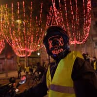 A masked \"yellow vest\" (Gilets jaunes) protester poses on a scooter near The Arc de Triomphe on the Champs Elysees in Paris Saturday during a rally against rising oil prices and living costs. Security forces in Paris fired tear gas and water cannon to disperse protesters. | AFP-JIJI