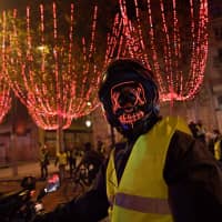 A masked \"yellow vest\" (Gilets jaunes) protester poses on a scooter near The Arc de Triomphe on the Champs Elysees in Paris Saturday during a rally against rising oil prices and living costs. Security forces in Paris fired tear gas and water cannon to disperse protesters. | AFP-JIJI