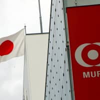 Japan\'s national flag is seen behind the logo of Mitsubishi UFJ Financial Group Inc (MUFG) at a bank branch in Tokyo last fall. | REUTERS