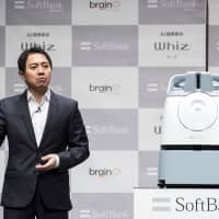 Fumihide Tomizawa, president and chief executive officer of SoftBank Robotics Group Corp., speaks next to a Whiz autonomous floor-cleaning robot during a news conference in Tokyo on Monday. | BLOOMBERG
