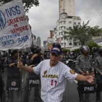 A state employee shouts slogans during a demonstration demanding salary improvements from the Venezuelan government as police block their way in Caracas Wednesday. | AFP-JIJI