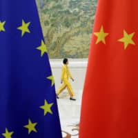 An attendant walks past EU and Chinese flags ahead of the EU-China High-level Economic Dialogue at the Diaoyutai State Guesthouse in Beijing on June 25, 2018. | REUTERS