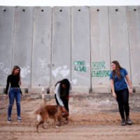 Israeli teens Meshy Elmkies, 16 (right), Liam Yefet, 16 (center) and Lee Cohen, 17, co-managers of the Otef.Gaza Instagram account, play with a dog near a barrier which borders the Gaza Strip in Kerem Shalom kibbutz in southern Israel earlier this month. | REUTERS