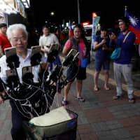 Neighbors watch Chen San-yuan, 70, known as \"Pokemon grandpa,\" as he plays the mobile game \"Pokemon Go\" near his home with 15 mobile phones, in a Taipei suburb on Monday. | REUTERS