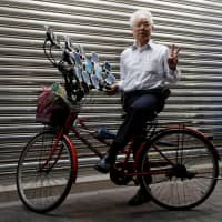 Chen San-yuan, 70, known as \"Pokemon grandpa,\" poses with his bicycle as he plays the mobile game \"Pokemon Go\" near his home with 15 mobile phones, in a Taipei suburb on Monday. | REUTERS