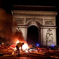 A protester is seen next to a burning barricade during a \"yellow vest\" protests against higher fuel prices held on the Champs-Elysees in Paris on Saturday. | REUTERS