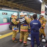 Firefighters are seen near a bullet train at Omiya Station in Saitama Prefecture on Friday. Smoke coming from a mobile battery carried by a passenger halted operations on the line. | KYODO