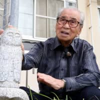 Yoshinori Kato, 90, talks about his A-bomb experience while touching the statue of Jizo, the guardian of children, which he donated to Danbara Elementary School. | CHUGOKU SHIMBUN