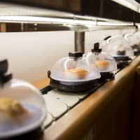 Plates of sushi covered with domes move along a conveyor belt at a Kura Corp. restaurant in Osaka. | BLOOMBERG