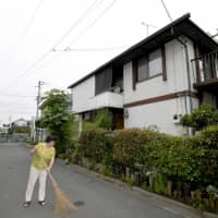 A woman cleans up the road behind her house in the city of Nishi-tokyo, as she started licensed private lodging in June. | KYODO