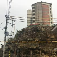 A cliff at the foot of prefectural housing in the Mizugama district of Kadena, Okinawa Prefecture, has a high risk of rockfalls, but the prefectural government cannot proceed with repair work because of unclaimed graves carved into it. | THE OKINAWA TIMES
