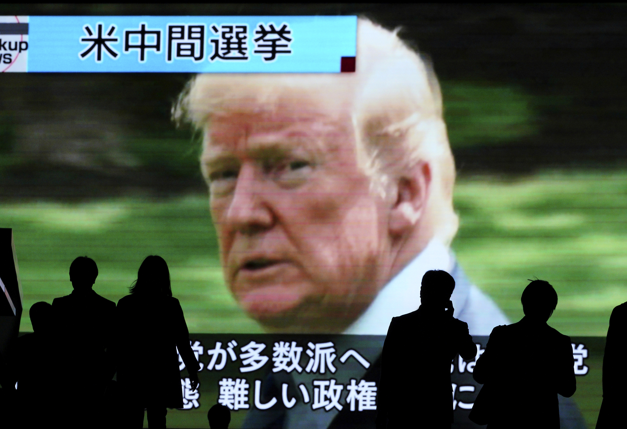 People walk past a huge public TV screen in Tokyo on Wednesday showing a news program covering the U.S. midterm elections. | AP