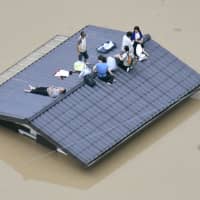 People wait to be rescued from the roof of an inundated house in the Mabi district of Kurashiki, Okayama Prefecture, on July 7. Torrential rains during the period caused substantial damage in several prefectures of western Japan. | KYODO
