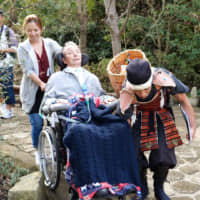 Tomoya Takano (right), the creator of a tour for people with disabilities, helps Hiroshi Matsuyama, who has ALS, navigate a bumpy path at Hase Temple in Kamakura, Kanagawa Prefecture, on Oct. 14. | CHISATO TANAKA