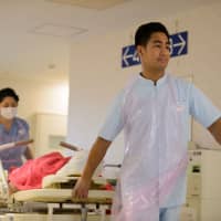 A Filipino care worker moves a patient at Eisei Hospital in Tokyo in December 2016. The Abe administration has proposed a bill that would reform foreign labor regulations to help ease Japan\'s growing manpower shortage. | BLOOMBERG