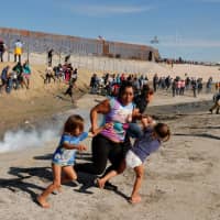 Members of a migrant family, part of a caravan of thousands traveling from Central America to the United States, run away from tear gas, fired by U.S. agents, in front of the border wall between the U.S and Mexico in Tijuana, Mexico, on Sunday. | REUTERS