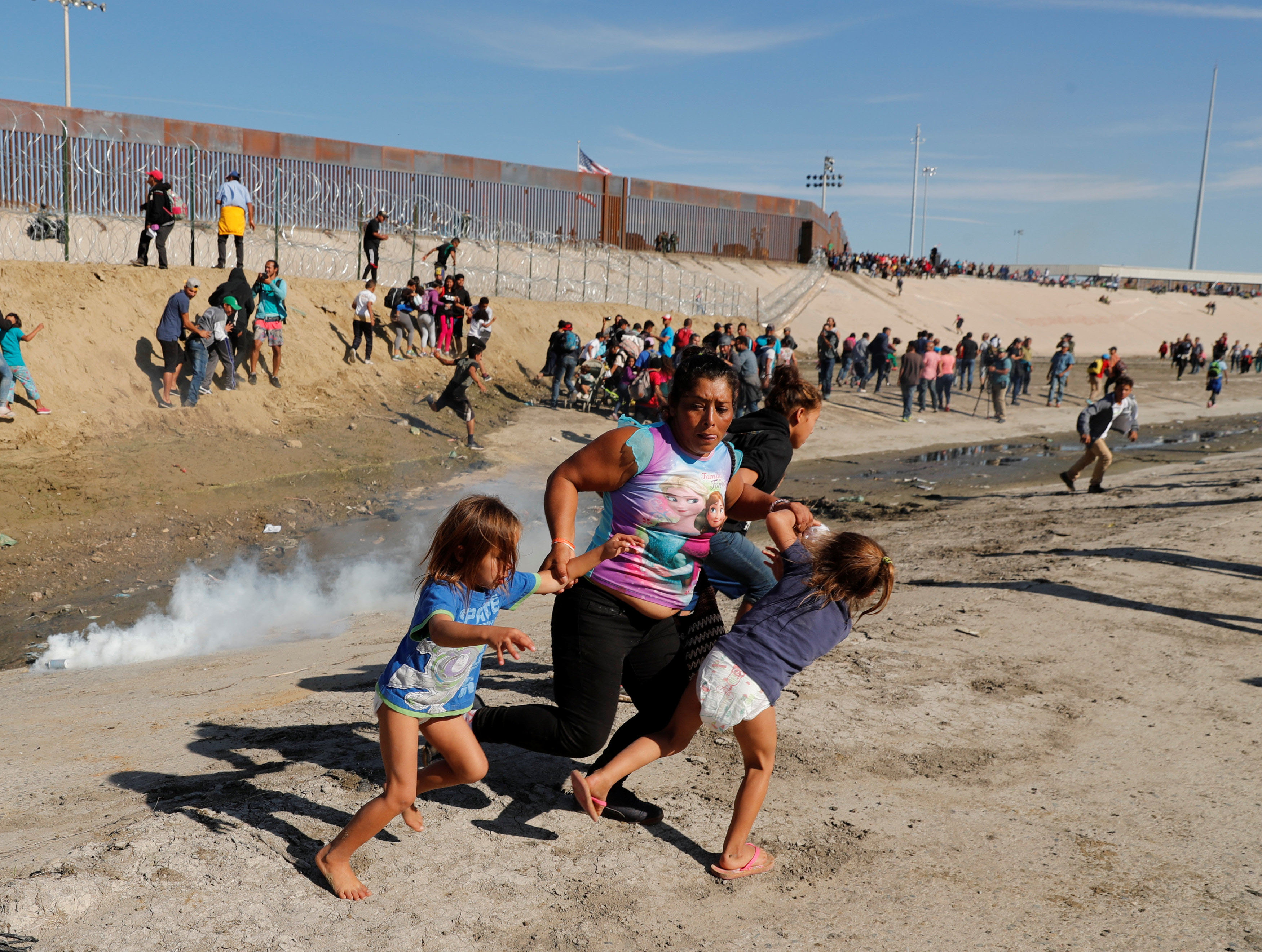 Members of a migrant family, part of a caravan of thousands traveling from Central America to the United States, run away from tear gas, fired by U.S. agents, in front of the border wall between the U.S and Mexico in Tijuana, Mexico, on Sunday. | REUTERS