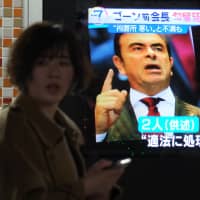 Pedestrians walk past a television screen showing a news program featuring former Nissan chief Carlos Ghosn in Tokyo on Friday. | AFP-JIJI