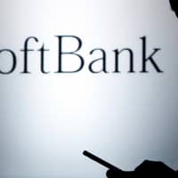 A pedestrian holding a mobile phone walks past a logo of SoftBank Corp in front of its branch in Tokyo in 2013. | REUTERS