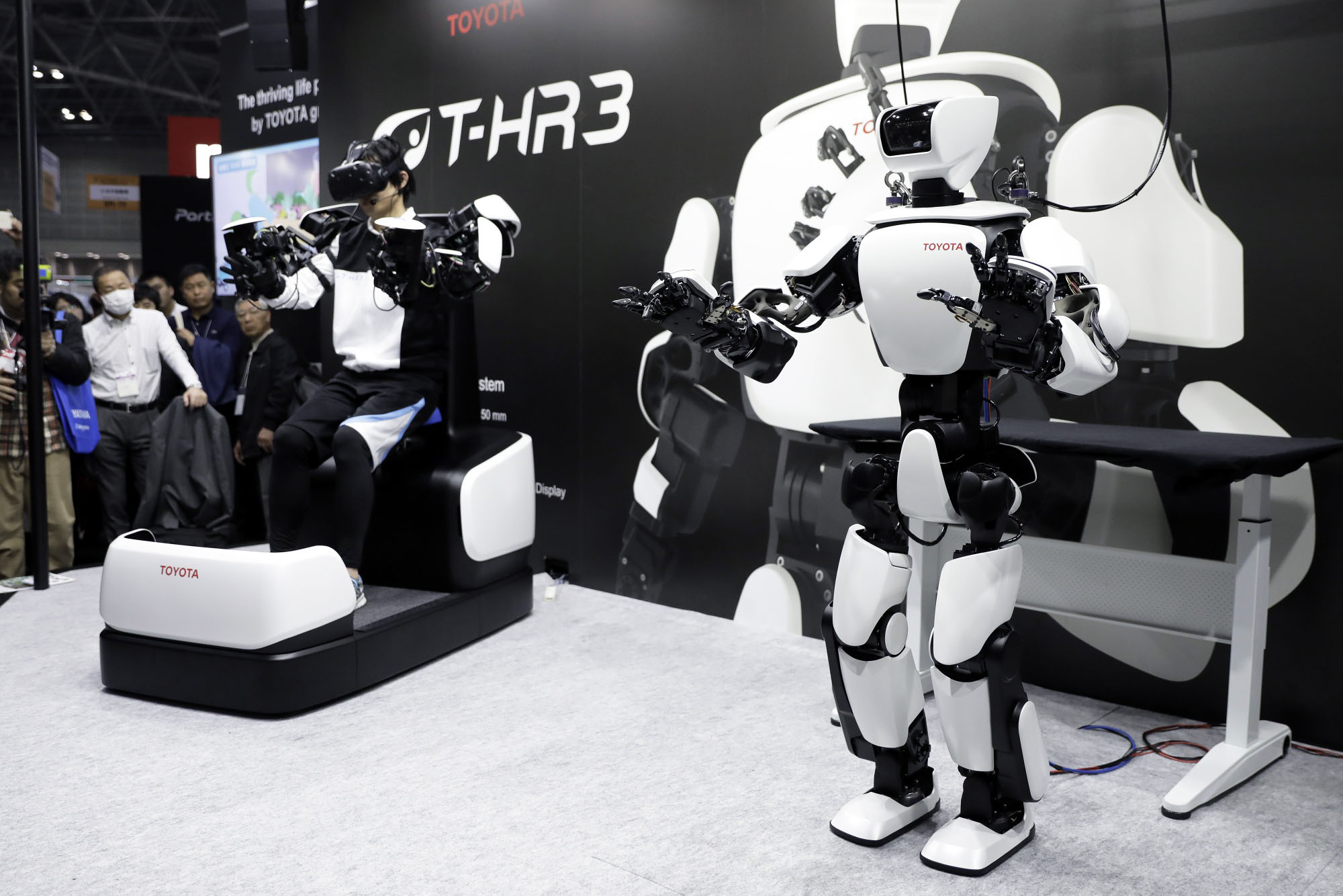An attendant operates Toyota Motor Corp.'s T-HR3 humanoid robot (right) from a remote maneuvering system (left) during a demonstration at the International Robot Exhibition in Tokyo in November 2017. | BLOOMBERG