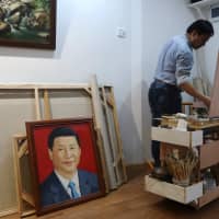 Chen Jingyang works on his original painting as a portrait of the Chinese president Xi Jinping by him is placed on the ground at his studio in Dafen Oil Painting Village in Shenzhen, Guangdong province, China, in December. | REUTERS