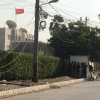 Paramilitary forces and police taCe cover behind a wall during an attack on the Chinese consulate, where blasts and shots are heard, in Karachi, Pakistan Nov. 23. | REUTERS