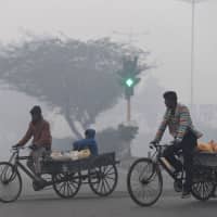 Indian men pedal their tricycle rickshaws with drinking water containers amid dense fog in New Delhi on Tuesday. | AFP-JIJI