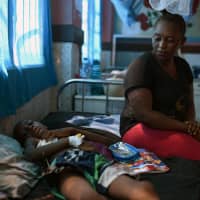 Khadija Kamara sits next to her son, Carlos, who she says hasn\'t been seen by staff at Freetown\'s Connaught Hospital in days, despite needing surgery to remove a foreign object lodged in his windpipe, in Freetown Wednesday. | REUTERS
