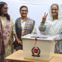 Bangladeshi Prime Minister Sheikh Hasina (right) flashes the victory symbol after casting her vote, as her daughter Saima Wazed Hossain (left) and her sister Sheikh Rehana (center) look on at a polling station in Dhaka on Sunday. | AFP-JIJI