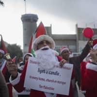 Palestinian protesters, some dressed as Santa Claus, carry Palestinian flags and chant anti Israel slogans during a protest in front of an Israeli checkpoint, in the West Bank city of Bethlehem Sunday. Christians around the world will celebrate Christmas on Monday. | AP