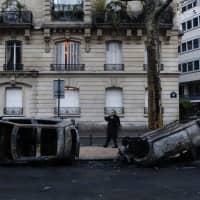 A man takes a snapshot Sunday of charred cars the day after a demonstration near the Arc de Triomphe in Paris. A protest over rising taxes and the high cost of living turned into a riot in the French capital, as activists torched cars, smashed windows, looted stores and tagged the Arc de Triomphe with multi-colored graffiti. | AP