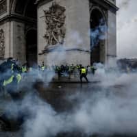 Demonstrators clash with riot police at the Arc de Triomphe during a protest of Yellow vests (Gilets jaunes) against rising oil prices and living costs, on Saturday in Paris. Speaking at the Paris police command center, France\'s prime minister said 36,000 people were protesting across France, including 5,500 in the capital for this third nationwide day of blockade and demos. | AFP-JIJI