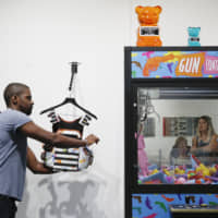 A gallery worker adjusts a child-size \"bullet proof\" vest as a woman looks at an art installation by WhlsBe called \"Gun Control\" at the Scope Miami Beach gallery during Art Basel on Thursday in Miami Beach, Florida. | AP