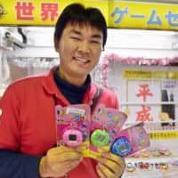 Naoya Igarashi, manager of Game Center Everyday in Gyoda, Saitama Prefecture, holds prizes for a claw machine last week. The machine features goods that bring back memories of earlier days in the Heisei Era. | KYODO