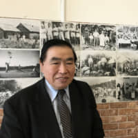 Joao Toshiei Masuko poses at his Brazilian shop and restaurant in Hamamatsu, Shizuoka Prefecture, on Dec. 14. In the background are a number of photos from a documentary about Japanese-Brazilians. | SAKURA MURAKAMI