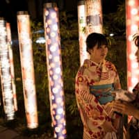 Women wearing kimono stand beside illuminated poles displaying kimono patterns at Randen Saga Station in Kyoto\'s Arashiyama tourism area on Dec. 8. | AFP-JIJI