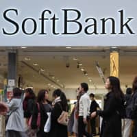 Dialing a prayer: People walk in front of a SoftBank outlet in Tokyo in November. | AFP-JIJI