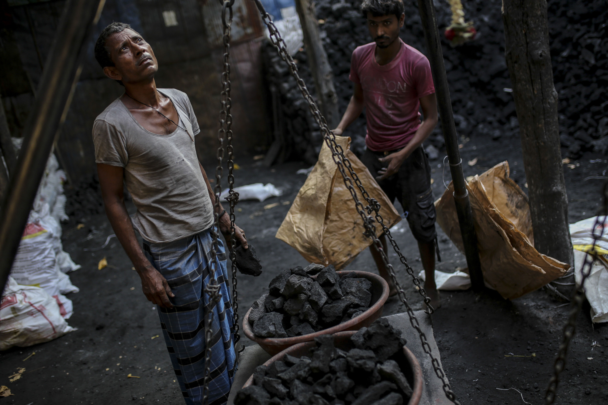 Workers weigh bowls of coal at a coal wholesale market in Mumbai. India is making a gradual shift away from fossil fuels, but coal is also getting a renewed push as a cheap source of energy. | BLOOMBERG