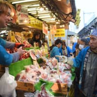 A customer listens to a clerk explain the benefits of eating octopus, on sale at a seafood shop in the Ameyoko market street in Taito Ward, Tokyo, on Friday. More than 1 million people are expected to visit the area, near Ueno Station, through Monday to buy groceries ahead of the New Year\'s holidays. | SATOKO KAWASAKI
