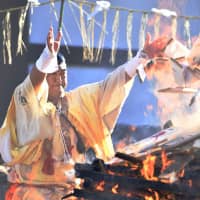 A priest throws amulets into a fire during an annual event at Naritasan Shinshoji temple in Narita, Chiba Prefecture, on Friday. About 20 priests burned a total of 50,000 amulets returned to the temple by visitors who had bought them in the past year, offering thanks for good health. | KYODO