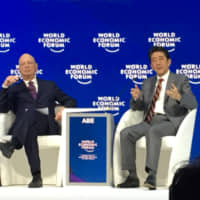 Prime Minister Shinzo Abe speaks as Klaus Schwab, a noted economist and the founder and executive chairman of the World Economic Forum, looks on during the WEF annual meeting in Davos on Wednesday. | SAYURI DAIMON