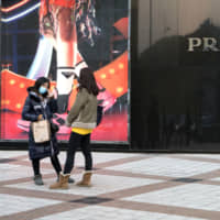 Pedestrians stand in front of a Prada SpA store in the Wangfujing shopping area of Beijing on Jan. 12. Some China watchers believe actual economic growth is already weaker than official data suggest. | BLOOMBERG