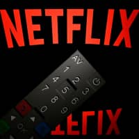 The logo of the Netflix entertainment company is displayed on a tablet screen with a remote control in front of it last year in Paris. Netflix unveiled plans Tuesday to boost prices for U.S. subscribers, a move that helped lift shares of the streaming television giant, which now faces an array of new competitors. | AFP-JIJI