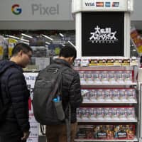 Customers look at a copy of the \"Super Smash Bros. Ultimate\" video game for the Nintendo Switch at a Bic Camera Inc. electronics store in Tokyo on Dec. 7 last year. | BLOOMBERG