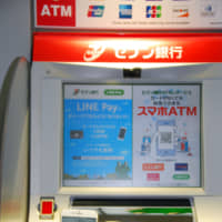 A customer shows a smartphone banking app in front of a Seven Bank ATM in October in Tokyo. The bank plans to add a facial recognition feature to the ATMs so people can instantly open bank accounts. | KYODO
