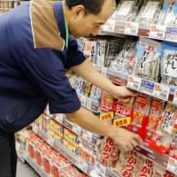 A shop employee arranges merchandise at a Tokyo supermarket. Government data released Friday show that households cut spending for the third straight month in November as unseasonably warm weather reduced the need for heating and winter clothing. | KYODO