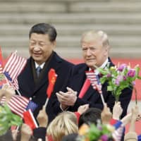 U.S. President Donald Trump and Chinese President Xi Jinping greet attendees waving American and Chinese flags during a welcoming ceremony outside the Great Hall of the People in Beijing in November 2017. | BLOOMBERG
