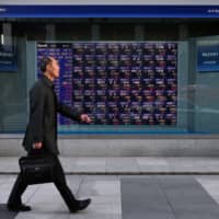 A pedestrian walks past an electronic stock board outside a securities firm in Tokyo on Friday. After the trade talks between the U.S. and China, some equity investors face a reality check and are taking a pause. | BLOOMBERG