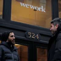 People stand outside a WeWork coworking space in New York City on Tuesday. WeWork Cos. will let investors and employees sell shares to SoftBank Group Corp. as part of the conglomerate\'s &#36;2 billion investment in the startup. | REUTERS